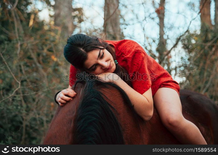 Beautiful young woman hugging brown horse and wearing dress