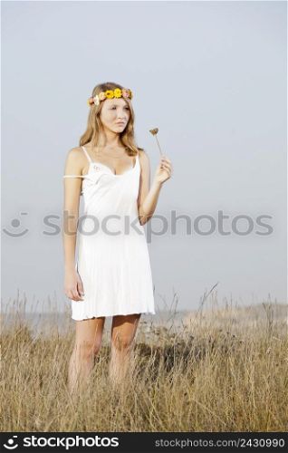 Beautiful young woman in a meadow holding a flower