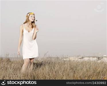 Beautiful young woman in a meadow holding and blowing flowers