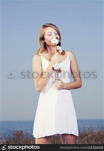 Beautiful young woman in a meadow holding and smelling a cotton plant