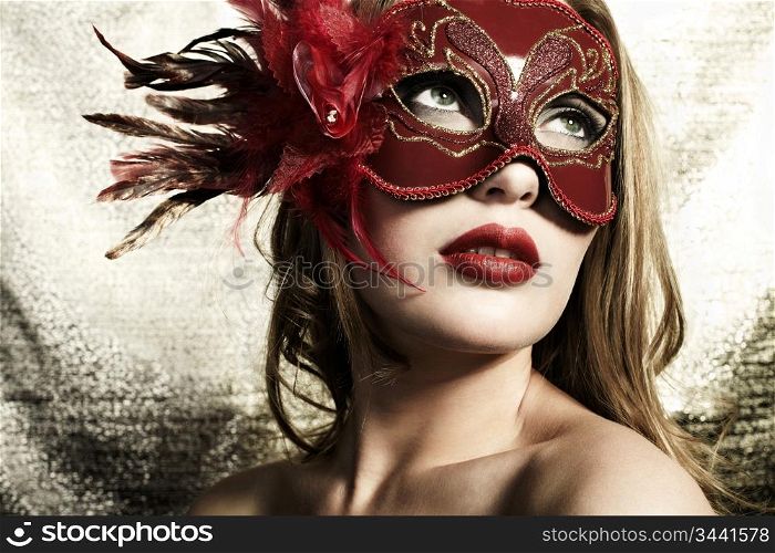 Beautiful young woman in a red mysterious venetian mask on a gold background