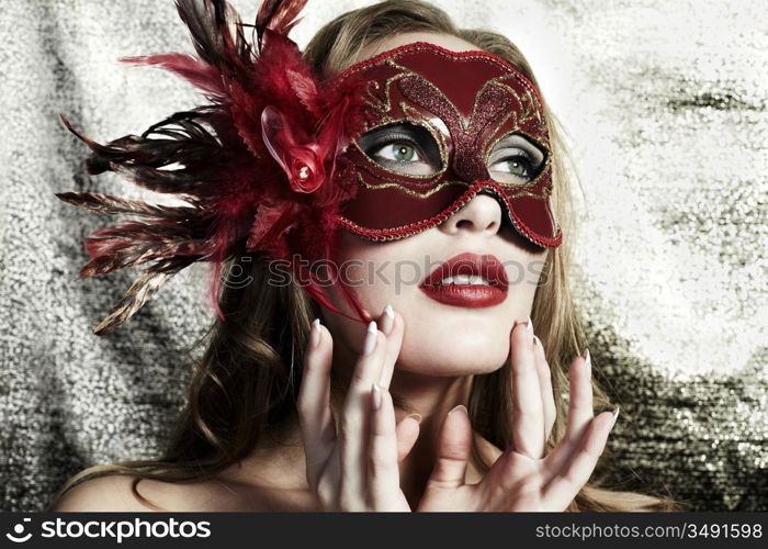 Beautiful young woman in a red mysterious venetian mask on a gold background