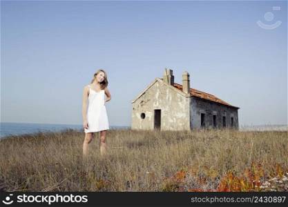Beautiful young woman in a white dress relaxing in a meadow close to a abandoned house