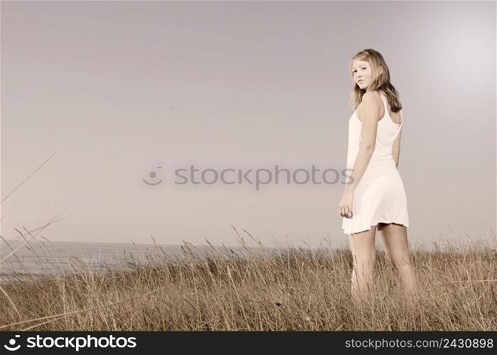 Beautiful young woman in a white dress relaxing in a meadow close to the sea