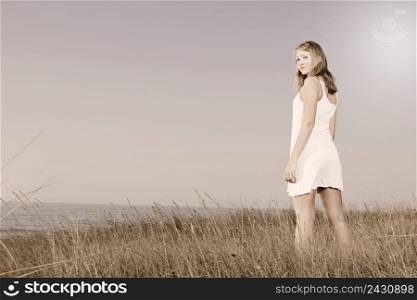 Beautiful young woman in a white dress relaxing in a meadow close to the sea