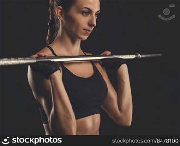 Beautiful young woman in a workout gear, lifting a barbell