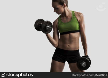 Beautiful young woman in a workout gear lifting dumbbells