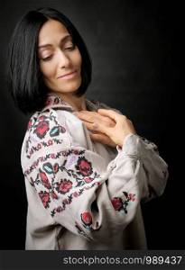 beautiful young woman in an embroidered ancient Ukrainian dress with a cross-stitch on a black background, linen clothes, look down