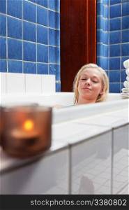 Beautiful young woman in bathtub at luxury spa with candle in glass