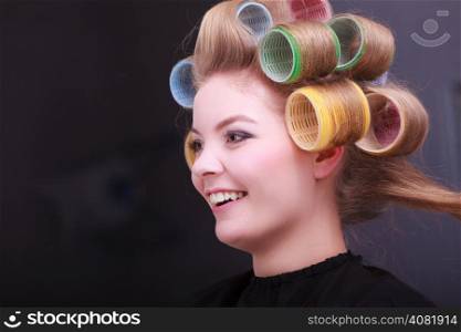 Beautiful young woman in beauty salon. Blond girl with hair curlers rollers by hairdresser. Hairstyle.