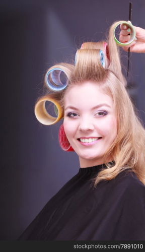 Beautiful young woman in beauty salon. Blond smiling girl with hair curlers rollers by hairdresser. Hairstyle.