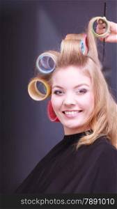Beautiful young woman in beauty salon. Blond smiling girl with hair curlers rollers by hairdresser. Hairstyle.