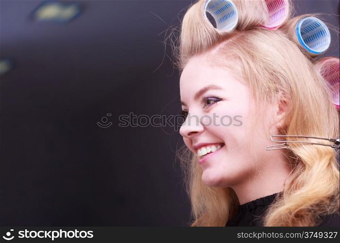 Beautiful young woman in beauty salon. Happy blond girl with hair curlers rollers by hairdresser. Hairstyle.