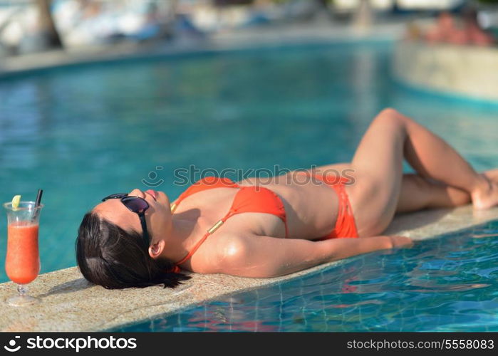 Beautiful young woman in bikini lying on a deckchair with a drink by the sea swimming pool and relax