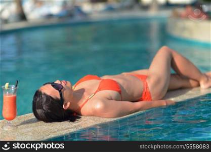 Beautiful young woman in bikini lying on a deckchair with a drink by the sea swimming pool and relax