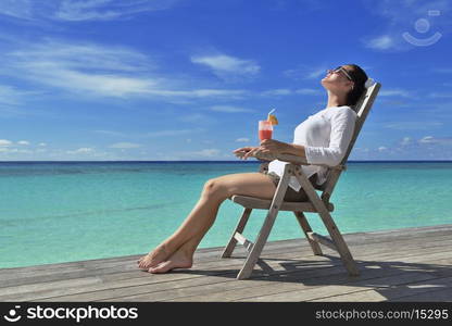 Beautiful young woman in bikini lying on a deckchair with a drink by the sea