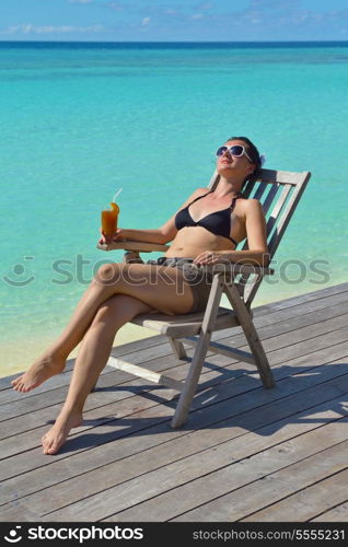 Beautiful young woman in bikini lying on a deckchair with a drink by the sea