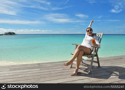 Beautiful young woman in bikini lying on a deckchair with a drink by the sea