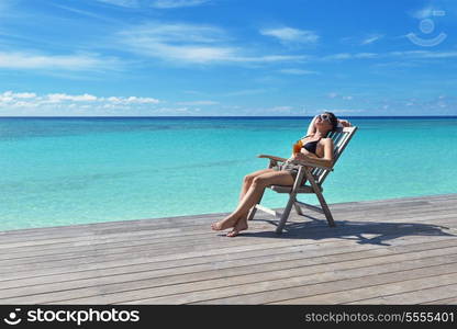 Beautiful young woman in bikini lying on a deckchair with a drink by the sea