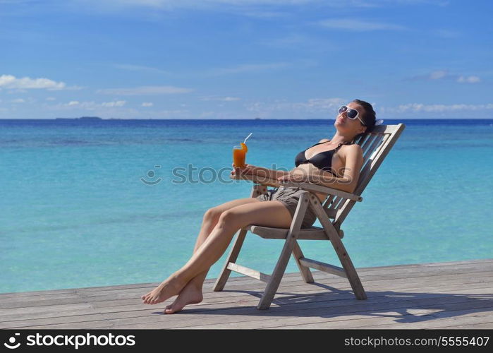 Beautiful young woman in bikini lying on a deckchair with a drink by the sea