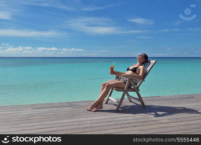 Beautiful young woman in bikini lying on a deckchair with a drink by the sea