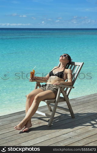 Beautiful young woman in bikini lying on a deckchair with a drink by the sea