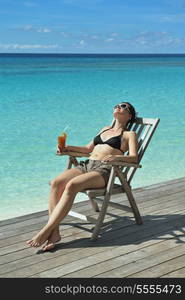 Beautiful young woman in bikini lying on a deckchair with a drink by the sea