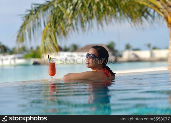 Beautiful young woman in bikini lying on a deckchair with a drink by the sea