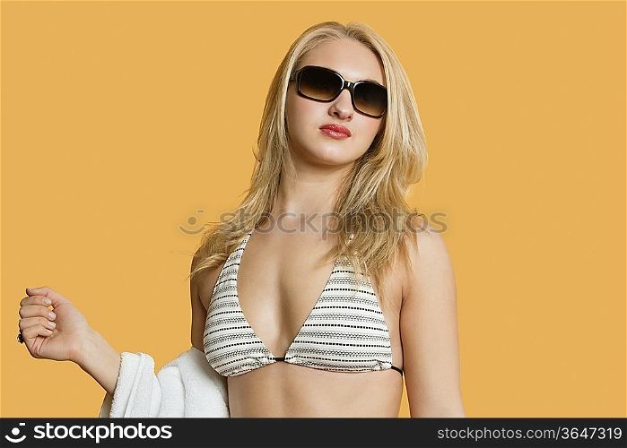 Beautiful young woman in bikini with towel in hand over colored background