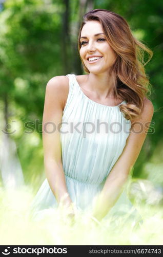 beautiful young woman in blue dress sitting on grass. young woman in blue dress sitting on grass. young woman in blue dress sitting on grass