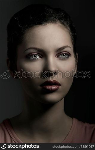 beautiful young woman in close-up portrait with red make-up, brown hair and green eyes in dark light