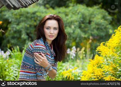 Beautiful young woman in colorful dress, against green of summer park