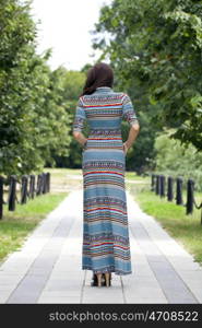 Beautiful young woman in colorful dress, against green of summer park