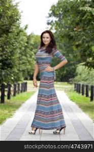 Beautiful young woman in colorful dress, against green of summer park