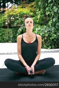Beautiful young woman in earphones doing yoga exercise outdoors