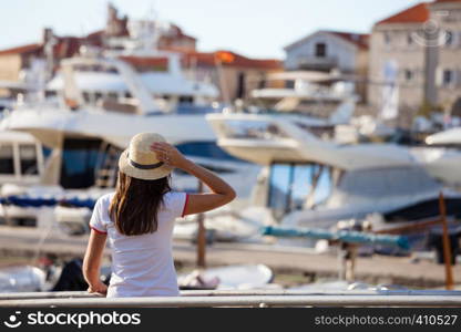 Beautiful young woman in hat standing close to the boats at Mediterranean city marina port.