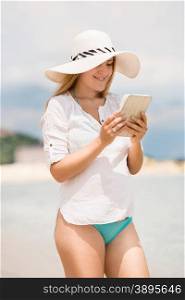 Beautiful young woman in hat working on digital tablet at beach