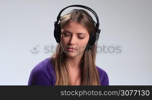 Beautiful young woman in headphones keeping eyes closed swaying to the beat of love song on white. Attractive brunette teenage girl with headset enjoying the music, touching earcups with both hand and moving groovily to the beat.