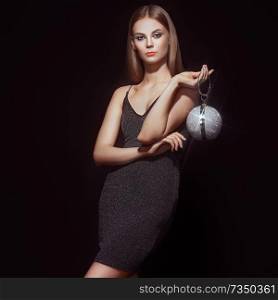Beautiful young woman in Little black dress. Girl posing on a black background. Blonde girl with long healthy and shiny hair. Care and Beauty. Fashion photo. Glamour lady with a handbag of shiny gems