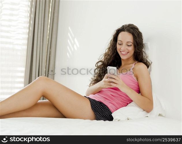 Beautiful young woman in lying on the bed and sending tect messages