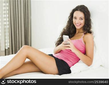Beautiful young woman in lying on the bed and sending tect messages