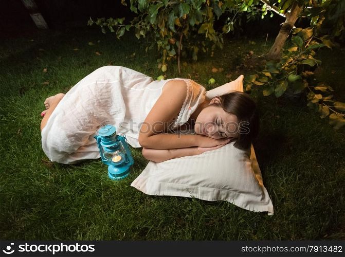 Beautiful young woman in nightgown sleeping on grass at garden at night
