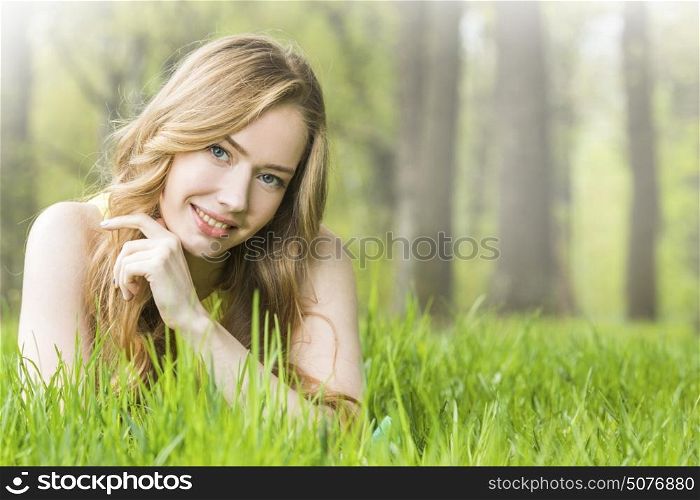 Beautiful young woman in park. Redhead or blonde romantic beautiful young woman laying on grass in park