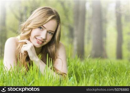 Beautiful young woman in park. Redhead or blonde romantic beautiful young woman laying on grass in park