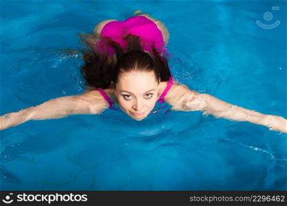 Beautiful young woman in pink swimsuit swimming in blue pool. Young female swimmer at holiday resort. Sport activity health concept.. Beautiful woman swimming in pool