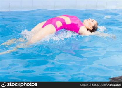 Beautiful young woman in pink swimsuit swimming in blue pool on her back. Young female swimmer at holiday resort. Sport activity health concept.. Woman in pink swimsuit swimming in blue pool on her back