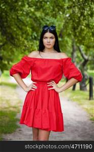 Beautiful young woman in red dress, against green of summer park