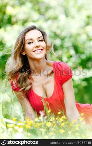 Beautiful young woman in red dress sitting on grass. Woman in red dress sitting on grass