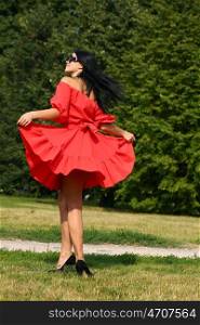 Beautiful young woman in red dress walking in summer park
