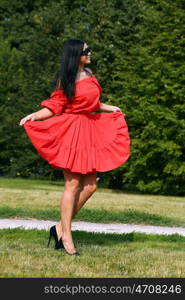 Beautiful young woman in red dress walking in summer park